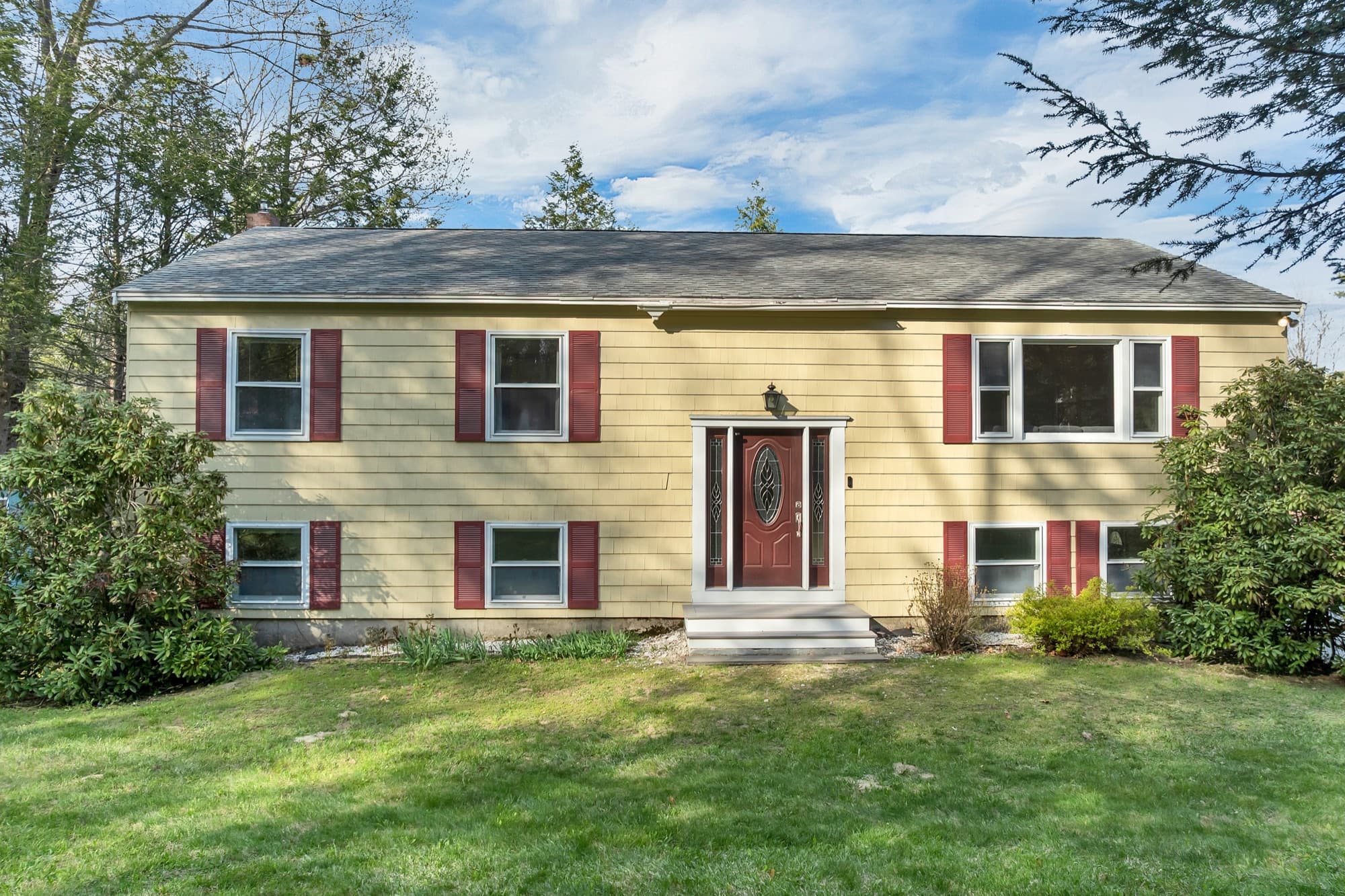 Front elevation, yellow siding with dark red shutters and a leaded-glass front door